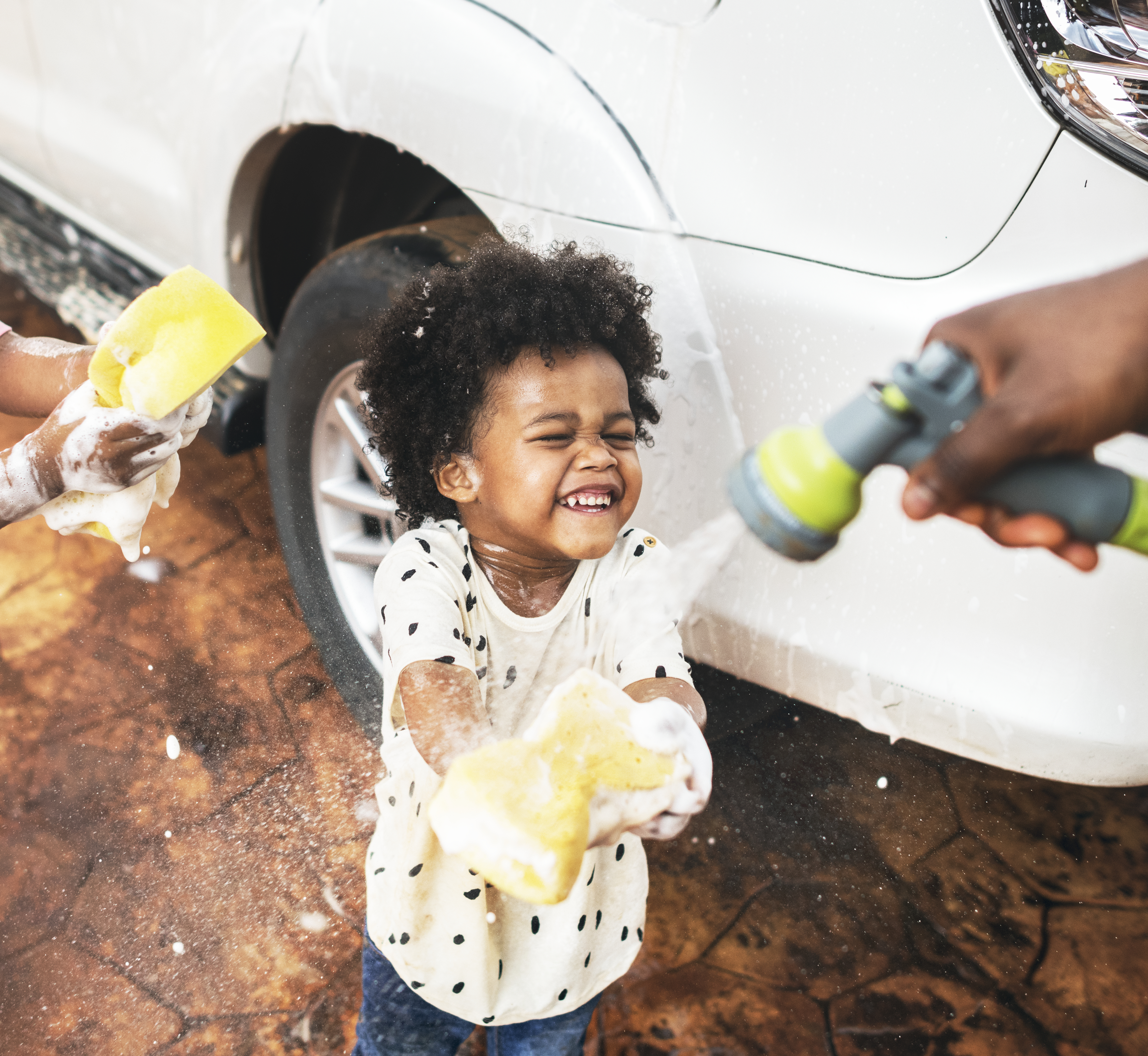young boy washing the family car getting sprayed with water by adult
