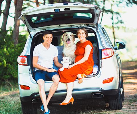 Man, woman, child, with a dog sitting in the trunk of their car